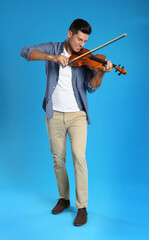 Fototapeta premium Happy man playing violin on light blue background