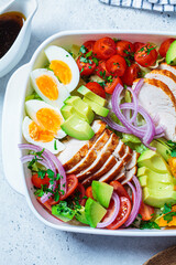 American cobb salad with chicken, avocado, egg, tomatoes and onions in white dish, top view. American cuisine concept.