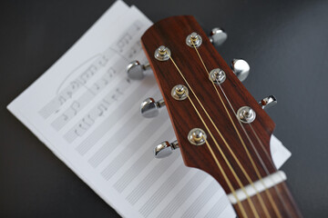 songwriting and musical instruments concept - close up of acoustic guitar head with music book