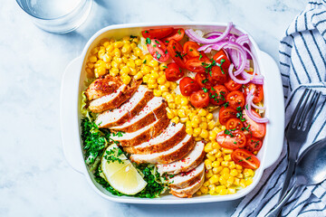 Healthy food concept. Diet chicken salad with corn, tomatoes and red onions in a white dish on white marble background.