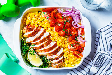 Fitness food concept. Diet chicken salad with vegetables and sports equipment on a white marble background.