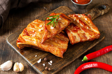 Cooked smoked pork ribs on a wooden serving board on a brown wooden table. Fried smoked pork ribs
