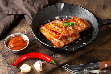 Boiled smoked pork ribs in a black cast-iron skillet on a brown wooden table. Fried pork ribs
