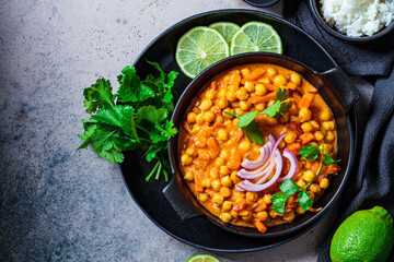 Vegan chickpea curry with rice and cilantro in black plate, dark background. Indian cuisine concept.