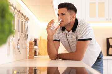 Fototapeta na wymiar Man drinking glass of pure water at countertop in kitchen