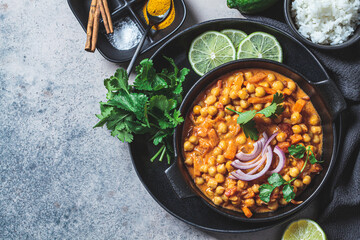 Vegan chickpea curry with rice and cilantro in black plate, dark background. Indian cuisine concept.