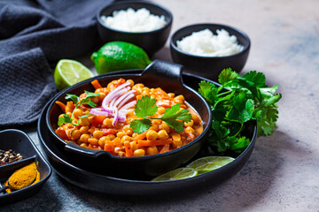 Vegan chickpea curry with rice and cilantro in black plate, dark background. Indian cuisine concept.