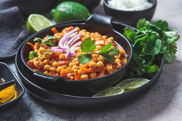 Vegan chickpea curry with rice and cilantro in black plate, dark background. Indian cuisine concept.