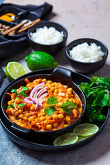 Vegan chickpea curry with rice and cilantro in black plate, dark background. Indian cuisine concept.