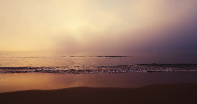 Ocean beach and foggy sunrise 4k video, waves splash on the sea sand