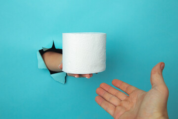 Female hand out of hole in the paperman, holding a roll of toilet paper. Isolate on blue background.