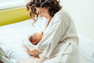 Brunette curly mother with her newborn baby boy at the hospital a day after a cesarean section...