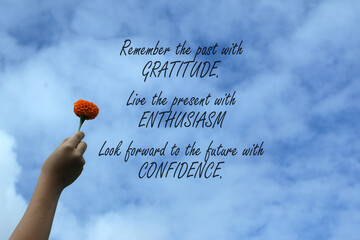 Inspirational quote - Remember the past with gratitude, live the present with enthusiasm, look forward to the future with confidence. With hand holding flower against bright blue sky background.