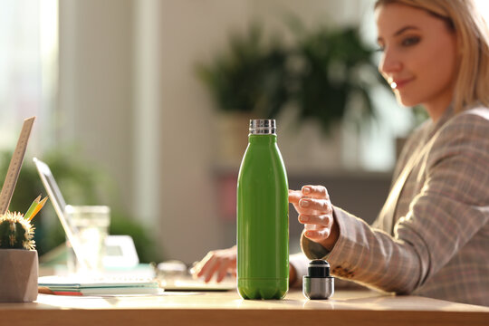 Woman taking green thermos bottle at workplace, closeup