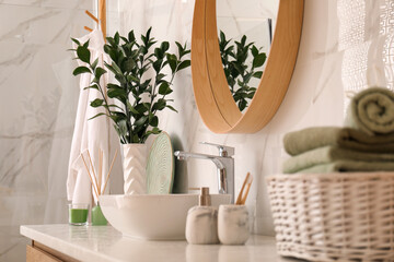 Vase with beautiful branches and toiletries near vessel sink in bathroom. Interior design