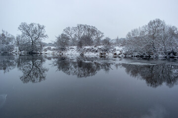 Frost cover trees and vegetation along frozen river in winter.