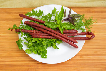 Long thin dry cured sausages on dish among the greens
