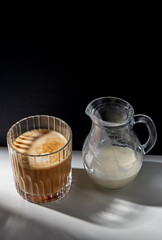 caffeine, objects and drinks concept - glass of coffee and jug with milk or cream on table