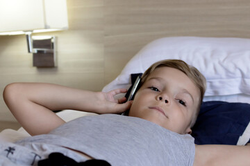 Little boy talking on the phone while lying down on bed.