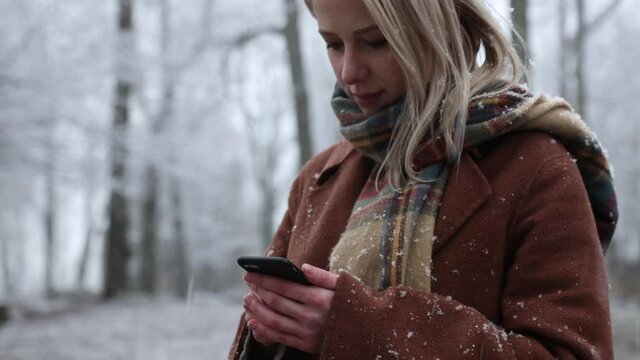 Woman in scarf and coat is using mobile phone in a snowfall