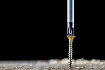 The screw and screwdriver close up on black background. Joinery and construction work.  - obrazy, fototapety, plakaty