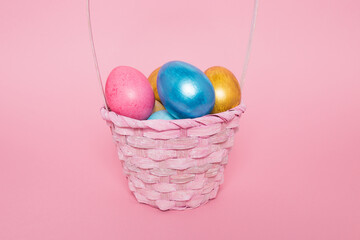 Multi-colored Easter eggs in a basket on a pink isolated background. Easter is a bright holiday.
