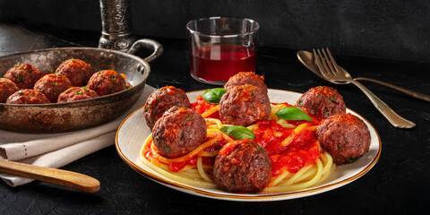 Meatballs and spaghetti panorama. Meatballs with tomato sauce, pasta, and basil on a dark background