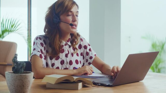 Female call center worker sitting desk focus on customer service member girl in headset looks at laptop screen write in notebook talk with client provide insurance information sell company product