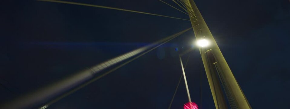 Night driving on cable-stayed Ada bridge in Belgrade, Serbia. Focused on height illuminated concrete pylon with stay cables. Car driver's point of view.