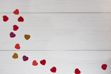 Top view frame of small red, shiny yellow and purple hearts made of paper scattered on a white old wooden background with copy space .Concept of texture, valentines day.