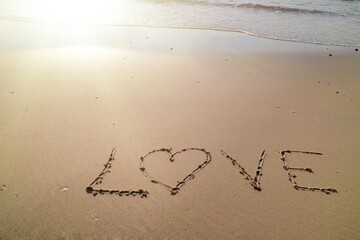 Text LOVE with the waves at the beach and sunlight in the summer morning. Nature and Valentine's day concept.