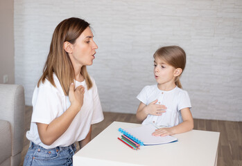 Young woman and little girl doing exercise for restructuring oral muscular phonetic targets.