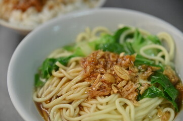 A bowl of dried noodles of traditional Taiwanese cuisine. The noodles are served with shallot confit and green vegetables.