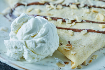 Pancakes with ice-cream, sprinkles, chocolate on the white plate in the dark background