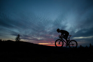 The silhouette of the cyclist on bike at sunset.A man ride on bike on the mountains. Sport and...