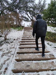 Hooded man climbing snowy stairs.