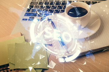 Double exposure of SEO writing and desktop with coffee and items on table background. Concept of search optimization.