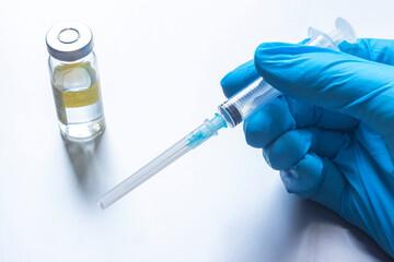 a hand with a medical glove on, holding a syringe and a vaccine on the table. the concept of...