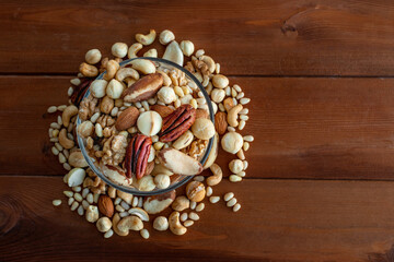 A mixture of nuts in a glass plate on a wooden table, a concept of healthy food, top view