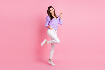 Full size photo of optimistic girl stand show v-sign wear lilac sweater trousers sneakers isolated on pink color background