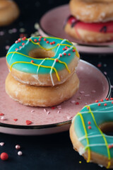 Donuts with multicolored icing sugar with various sugar sprinkles in stacks on pink plates. Sweet food background