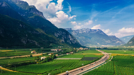Fototapeta premium Aerial Drone View: Beautiful Farmlands of Italy Located in the Mountains. Highway Lying in the Mountainous Region. Vineyards, Olive Trees, Various Vegetable Growing Fields and Agricultural Plantations
