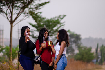 young beautiful african ladies taking a stroll in a garden, holding bottles of drink and having happy discussion