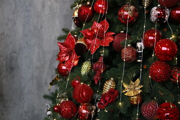 
beautiful New Year tree decorated with red and gold toys against a gray concrete wall in a luxury...