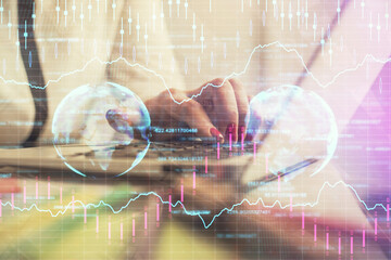 Double exposure of businesswoman hands typing on computer and financial graph hologram drawing....