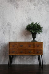 
a vase with pine needles on a wooden chest of drawers against a gray concrete wall