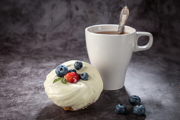 Tea in a white mug with a handle, a spoon, a cake with strawberries and blueberries on a gray background