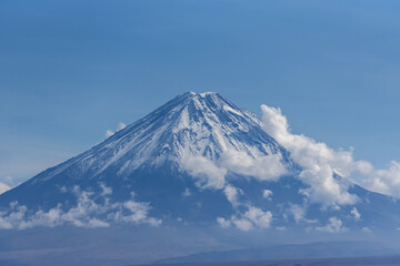 Majestic view of snowy volcanic mountain Licancabur surrounded by clouds on sunny day under blue sky
