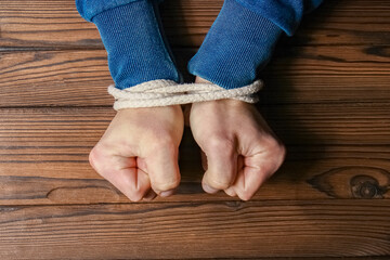 a Hands tied with a rope life-threatening on a wooden background. Slavery in business is human...