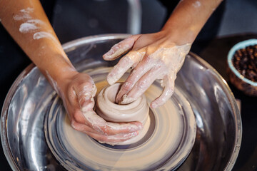 Close-up of the hands of a woman ceramist working with a potter's wheel in a cozy, bright workshop. A young experienced woman skillfully makes a mug, vase or plate. Creative people, pottery workshop